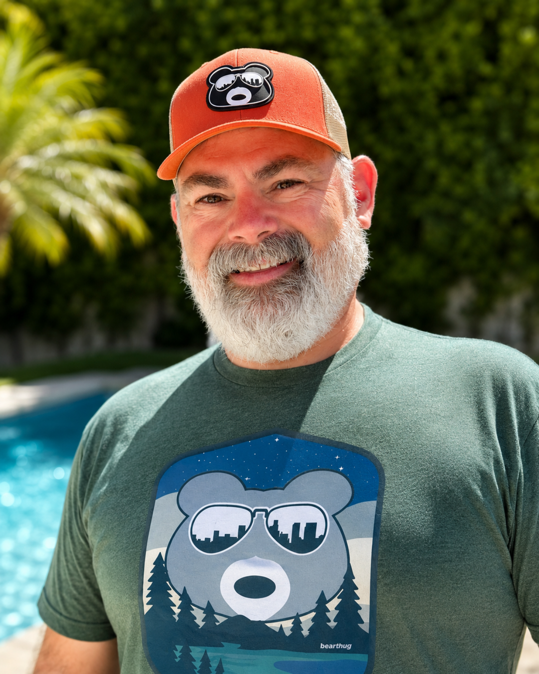 Man wearing an orange cap and green t-shirt with a bear graphic by a pool